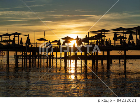 pier with umbrellas and sunbeds. silhouettes. beautiful sunset on sea.  84232021