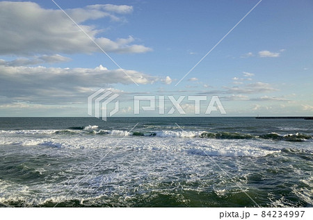 初冬の小春日和の午後の青い空と薄暗い雲と少し荒れた海 84234997