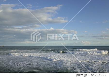初冬の小春日和の午後の青い空と薄暗い雲と少し荒れた海 84234999