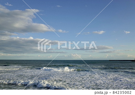 初冬の小春日和の午後の青い空と薄暗い雲と少し荒れた海 84235002
