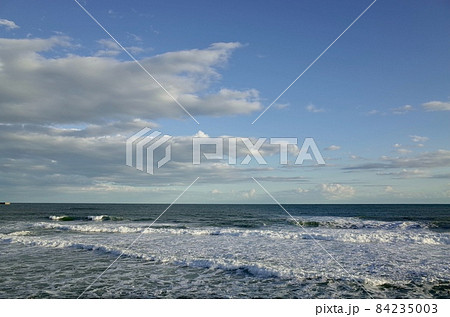 初冬の小春日和の午後の青い空と薄暗い雲と少し荒れた海 84235003