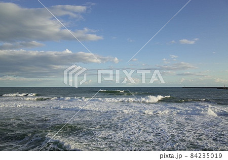 初冬の小春日和の午後の青い空と薄暗い雲と少し荒れた海 84235019