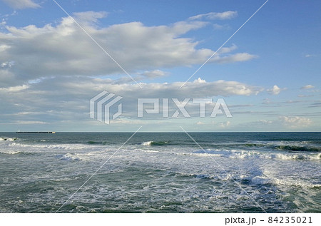 初冬の小春日和の午後の青い空と薄暗い雲と少し荒れた海 84235021