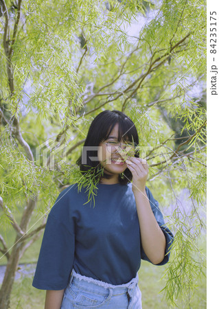 asian teenager standing under green tree leaves 84235175