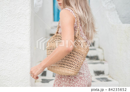 Picture of woven straw summer bag. Trendy summer outfit. Mock up. Blond woman in casual dress holding woven straw summer bag. High quality photo  84235652
