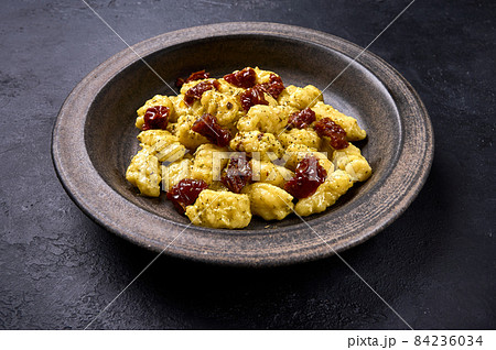 Close up potato gnocchi with parmesan and dried tomatoes in dark ceramic plate, low key Close up potato gnocchi with parmesan and dried tomatoes in dark ceramic plate, low key 84236034