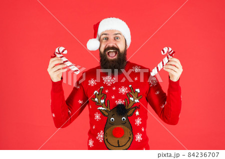 brutal hipster in winter knitted xmas sweater. mature guy with holiday candy stick brutal hipster in winter knitted xmas sweater. mature guy with holiday candy stick 84236707