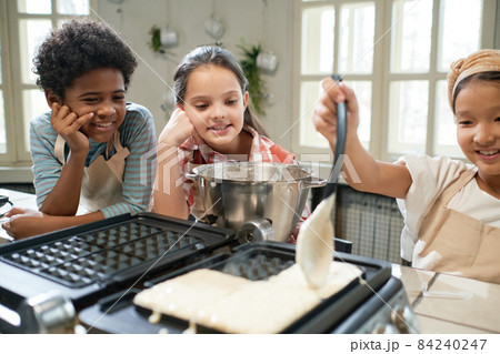 Girl putting dough on the waffle icon and learning to bake waffles with her friends in the kitchen 84240247