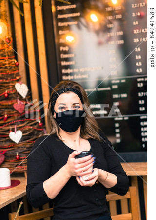 A sweet female of caucasian appearance in a black face mask, sits and works in an Internet cafe. A sweet female of caucasian appearance in a black face mask, sits and works in an Internet cafe. 84241583