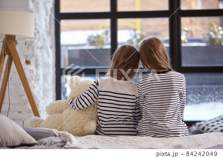The image of two little sisters sitting on the bed in the room. The image of two little sisters sitting on the bed in the room. 84242049