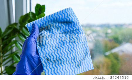 Employee hand in rubber protective glove holding dirty micro fiber cloth wiping window from dust. General spring cleaning. Housework and housekeeping concept 84242516