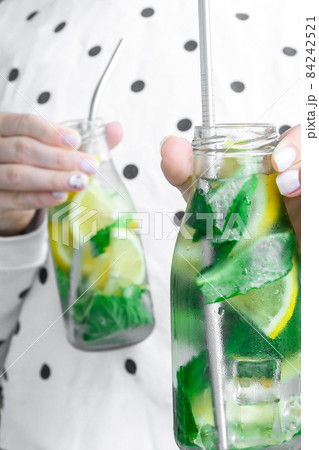 Female hand holding Mojito refreshing cocktail with eco metal drinking straw, alcohol drink. Lemonade with lemon and mint leaves. Summer refreshing detox drinks. Clean eating, healthy lifestyle 84242521