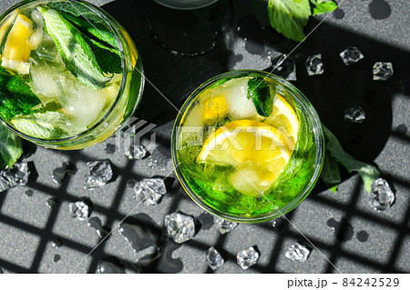Mojito refreshing cocktail, alcohol drink. Lemonade with lemon and mint leaves on dark background. Trendy shadows Ice cubes. Summer refreshing detox drinks. Clean eating, healthy lifestyle concept. 84242529