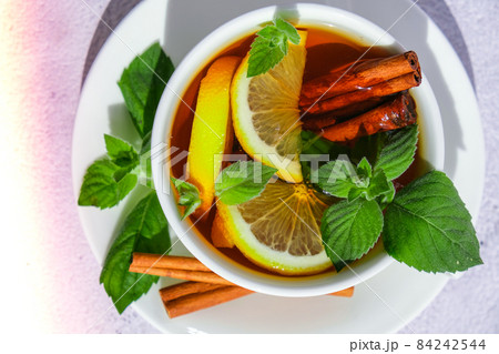 Black and green tea with lemon, cinnamon sticks and mint leaves. Hot drink. Healthy melissa tea natural organic aromatic drink in cup. Summer, Autumn winter warming drink. Black and green tea with lemon, cinnamon sticks and mint leaves. Hot drink. Healthy melissa tea natural organic aromatic drink in cup. Summer, Autumn winter warming drink. 84242544
