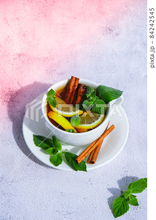 Black and green tea with lemon, cinnamon sticks and mint leaves. Hot drink. Healthy melissa tea natural organic aromatic drink in cup. Summer, Autumn winter warming drink. 84242545