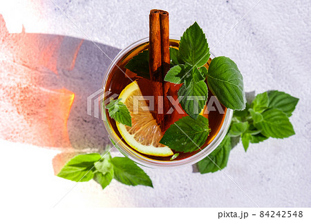 Black and green tea with lemon, cinnamon sticks and mint leaves. Hot drink. Healthy melissa tea natural organic aromatic drink in cup. Summer, Autumn winter warming drink. Black and green tea with lemon, cinnamon sticks and mint leaves. Hot drink. Healthy melissa tea natural organic aromatic drink in cup. Summer, Autumn winter warming drink. 84242548