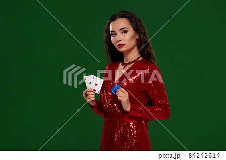 Young beautiful lucky brunette woman in a red evening dress, holds her cards, a pair of aces and chips on green background Young beautiful lucky brunette woman in a red evening dress, holds her cards, a pair of aces and chips on green background 84242614