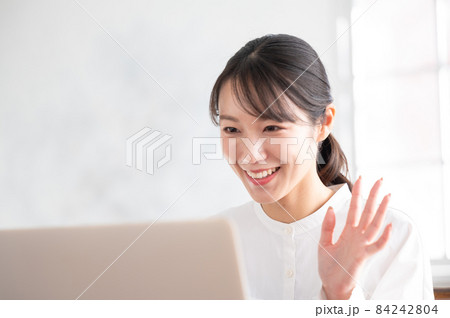 パソコンを使いながらZoomなどでリモートワークをする笑顔が美しい若い日本人女性左側にコピースペース 84242804