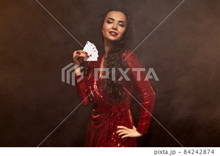Young beautiful lucky brunette in a red evening dress shows her cards, a four of aces Young beautiful lucky brunette in a red evening dress shows her cards, a four of aces 84242874