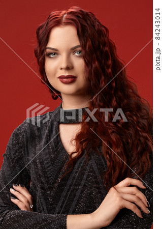 Beautiful sexy woman is posing in a knitted dress on a red background. Evening makeup. Long, healthy, red curly hair. Beautiful sexy woman is posing in a knitted dress on a red background. Evening makeup. Long, healthy, red curly hair. 84243014