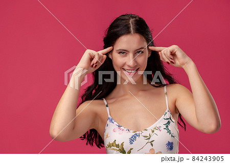 Portrait of a pretty young woman in a light dress standing on pink background in studio. People sincere emotions. Portrait of a pretty young woman in a light dress standing on pink background in studio. People sincere emotions. 84243905