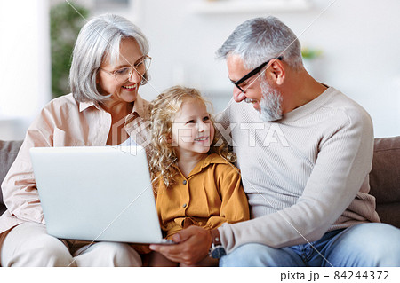 Smiling senior grandparents and cute little girl granddaughter watching cartoons on laptop Smiling senior grandparents and cute little girl granddaughter watching cartoons on laptop 84244372