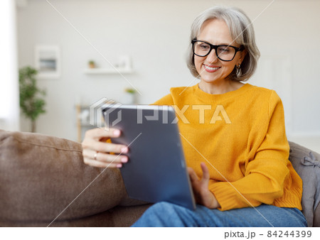 Portrait of happy smiling senior woman resting relaxing on sofa with tablet at home 84244399
