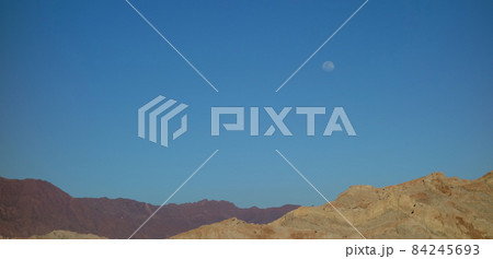 solitary moon at dusk, orange mountains and blue sky. desert landscape 84245693