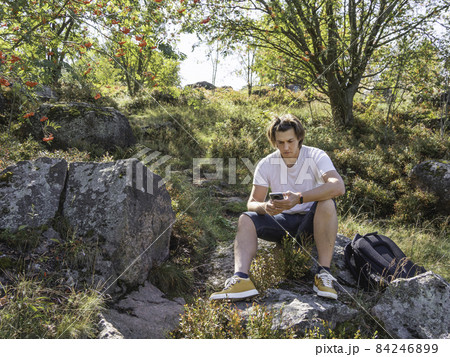 Frowning man looks at smartphone screen. Orientation on terrain using built-in navigator application. Hiking with backpack in fall season. Bright autumn leaves. 84246899