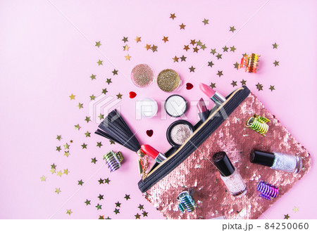 Bright composition of fashion accessories. Glitter sequins cosmetic bag with lipsticks, nail polishes and other objects. Object on soft pastel background with decorative tinsel. Flat lay, top view. Bright composition of fashion accessories. Glitter sequins cosmetic bag with lipsticks, nail polishes and other objects. Object on soft pastel background with decorative tinsel. Flat lay, top view. 84250060