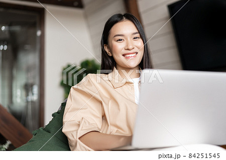 Smiling asian woman using laptop computer at home and looking happy at camera 84251545