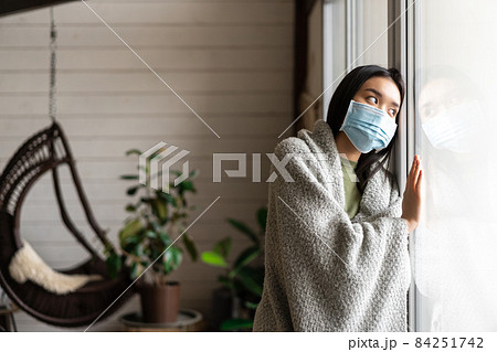 Sad asian girl in medical face mask looking outside window and yearning go for walk, being ill, catching covid 19 or flu Sad asian girl in medical face mask looking outside window and yearning go for walk, being ill, catching covid 19 or flu 84251742