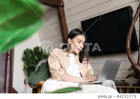 Image of excited asian girl sits at home with laptop, looking amazed at computer screen Image of excited asian girl sits at home with laptop, looking amazed at computer screen 84251773