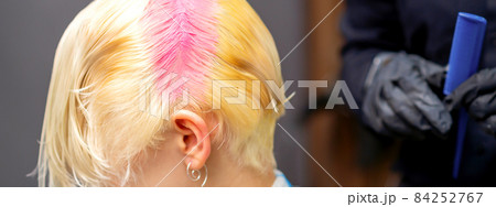 Young caucasian woman tints hair roots in pink color in a beauty salon. 84252767