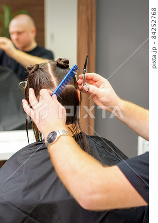 Male stylist cutting the hair of female client in professional beauty salon. Male stylist cutting the hair of female client in professional beauty salon. 84252768