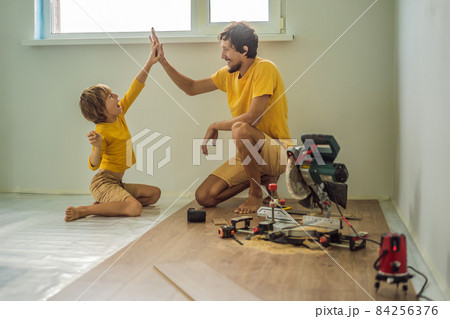 Father and son installing new wooden laminate flooring on a warm film floor. Infrared floor heating system under laminate floor 84256376