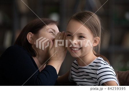 Close up happy grandmother with little granddaughter gossiping, sharing secrets Close up happy grandmother with little granddaughter gossiping, sharing secrets 84259395