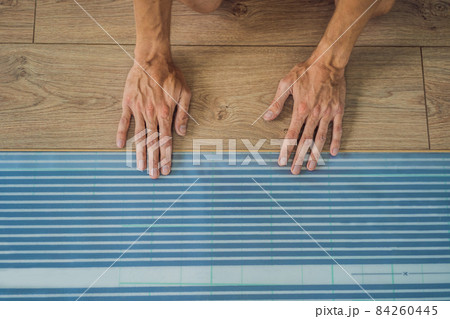 Man installing new wooden laminate flooring on a warm film floor. Infrared floor heating system under laminate floor Man installing new wooden laminate flooring on a warm film floor. Infrared floor heating system under laminate floor 84260445