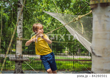Little boy in a rope park. Active physical recreation of the child in the fresh air in the park. Training for children Little boy in a rope park. Active physical recreation of the child in the fresh air in the park. Training for children 84260501