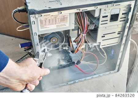 Cleaning an open dusty old computer with a compressed air gun 84263520