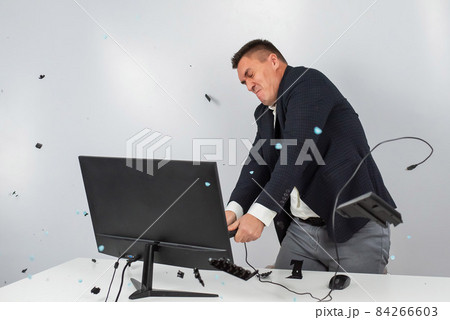Caucasian man in a suit gets angry and smashes the keyboard on the monitor. An office worker in a rage breaks the computer. Caucasian man in a suit gets angry and smashes the keyboard on the monitor. An office worker in a rage breaks the computer. 84266603