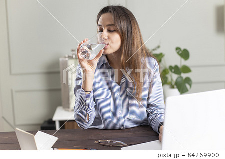 Freelancer young woman working at home and drinking water Freelancer young woman working at home and drinking water 84269900