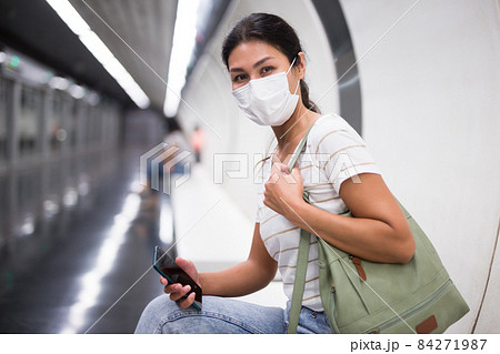 Woman in face mask with smartphone sitting on bench in subway station 84271987