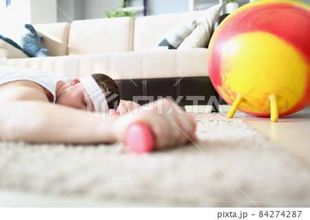 Tired man laying on carpet floor with dumbbell equipment in hand Tired man laying on carpet floor with dumbbell equipment in hand 84274287
