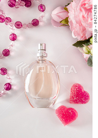 Bottle of perfume, flowers and hearts on a light background. Fragrant perfumes and delicate pink peonies on a light background. Gift for Valentine's Day, vertical photo. 84274786