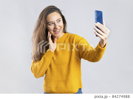 Portrait of cheerful girl smiling and taking selfie using mobile phone 84274988