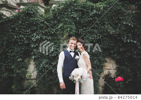 Stylish couple of happy newlyweds walking in the park on their wedding day with bouquet 84275014