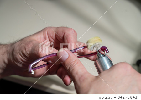 An optician technician polishes the frame of glasses. A professional optician fixes glasses. 84275843