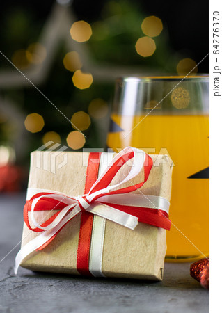 Christmas gift in craft paper and orange cocktail in glass with black stripes with golden bokeh. Christmas gift in craft paper and orange cocktail in glass with black stripes with golden bokeh. 84276370