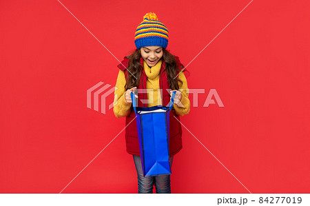 amazed child in winter clothes open shopping bag on red background, christmas shopping amazed child in winter clothes open shopping bag on red background, christmas shopping 84277019